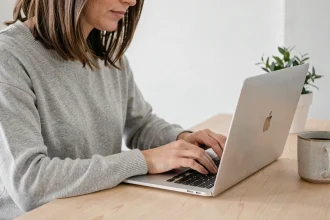 Femme utilisant un clavier Mac AZERTY pour taper le symbole tilde sur un MacBook posé sur un bureau en bois